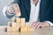 Business man puts next stone on complex structure made from wooden blocks; career or achievement or complex project management