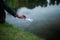 A business man putting a paper boat into water of lake.