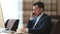 Business man sitting at table with computer and talking to mobile phone in lobby