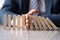 Business man in suit holding with hand falling sequence of wooden blocks