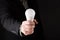 Business man in suit Holding a white light bulb in hand, isolated on gradient black background