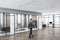 Business man walking in modern concrete glass office interior with daylight, equipment and wooden flooring. Workplace design