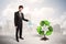 Business man watering green recycle sign tree on city background