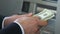 Business person counting dollars near ATM and putting money in wallet, banking