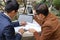 Business team sitting on marble in park and working with laptop , tablet and charts.