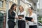 Business team with tablets posing outside office building. Three ladies looking directly on tablet screen