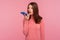 Business woman with brown hair in pink sweater holding mobile phone in hands and talking into load speaker, making voice note,