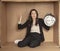 Business woman with a clock in hand sits in a cardboard office