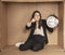 Business woman with a clock in hand sits in a cardboard office