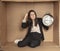 Business woman with a clock in hand sits in a cardboard office