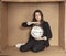 Business woman with a clock in hand sits in a cardboard office