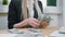 Business woman counting cash in hands. Crop view of female in elegant suit sitting at wooden desk and counting large