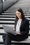 business woman in a formal suit with a laptop in an office or business center sits on the steps in the lobby and works