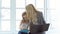 Business woman with laptop and little girl with tablet sitting by the big window