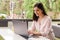 Business woman in pastel pink shirt working on laptop and making notices in her notebook in cafe at terrace