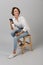 Business woman posing isolated over grey wall background sitting on stool using laptop computer chatting by phone