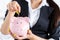 Business woman putting pin money coins into pink piggybank slot