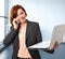 Business woman with red hair at work smiling with laptop computer talking busy on mobile phone