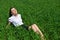 Business woman relaxing in green grass field outdoor under sun. Beautiful young girl dressed in suit resting, spring landscape, br