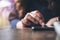 A business woman`s hand touching and sliding finger on a black smart phone on wooden table