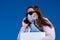 A business woman speaks on phone on street in medical mask during coronavirus pandemic against background of blue neb