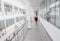 Business Woman Walking Along the Office Corridor. Smiling Businesswoman Goes Against White Offices Background. A young pretty girl