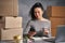 Business woman working from home with laptop and smartphone, preparing boxes with products for send