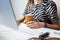 Business woman working in minimalistic office. Young female person with coffee in front of desktop computer at modern workplace