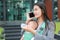 Business woman working by telephone with carrying her infant and feeding her child`s by milk bottle. Busy mother hurrying.