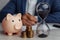 Businessman approves important contract in office. Pink piggy bank with stack of coins and hourglass on desk close-up