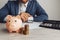 Businessman approves important contract. Pink piggy bank with stack of coins on desk. Economy, business and management