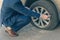 A businessman in a blue suit crouching near his car and checks the degree of damage to a punctured wheel. Hole in the tire.