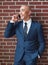 Businessman, brick wall and phone call in suit with smile for networking, contact and corporate connection. Happy worker