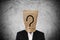 Businessman with brown paper bag on head, with question mark, on concrete texture background