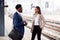 Businessman And Businesswoman Commuting To Work Talking On Railway Platform Waiting For Train