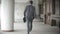 Businessman carrying briefcase while moving forward. Man in formalwear walking near modern office building, full length