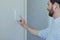 Businessman enters finger password lock code on alarm panel, on white wall, rear view of man with beard