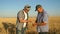 Businessman and farmer with tablet working as a team in field. agronomist and farmer are holding grain of wheat in their
