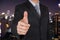 Businessman give a thumbs up for compliment on blur night cityscape background as business, praise, congratulate, good and like