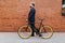 Businessman going to work by bicycle agaist brick wall. Handsome man enjoying city ride by bicycle. Young businessman with his