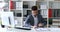 Businessman in gray jacket sitting at table in white office, signing document and making paper airplane