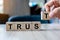 Businessman hand holding wooden cube block with TRUST business word on table background. Trustworthy, Truth, beliefs and agreement