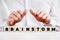 Businessman holding his hands protectively over the wooden cubes with the word brainstorm