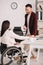 Businessman holding smartphone while standing near disabled businesswoman in office