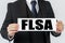 A businessman holds a sign in his hands which says FLSA