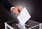 Businessman inserting ballot in box on desk