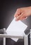 Businessman inserting ballot in box on desk