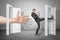 Businessman kicking a door and big hand appearing out of an open door on grey wall background