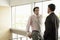 Businessman Looking At Male Colleague By Railing In Office