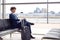 Businessman With Luggage Sitting In Airport Departure Lounge Looking Out Of Window